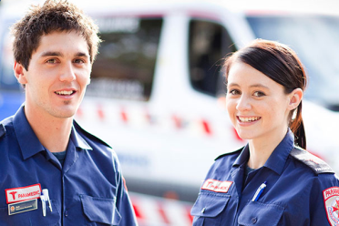 A young male and female paramedic standing in front of an ambulance.